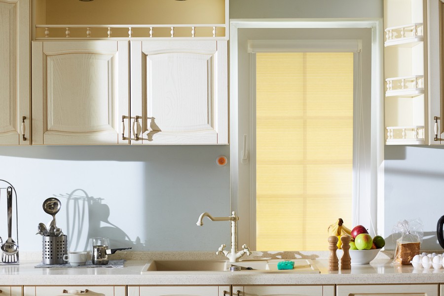 View of a white kitchen counter with white cabinets, the window above the sink fitted with a custom motorized shade. 