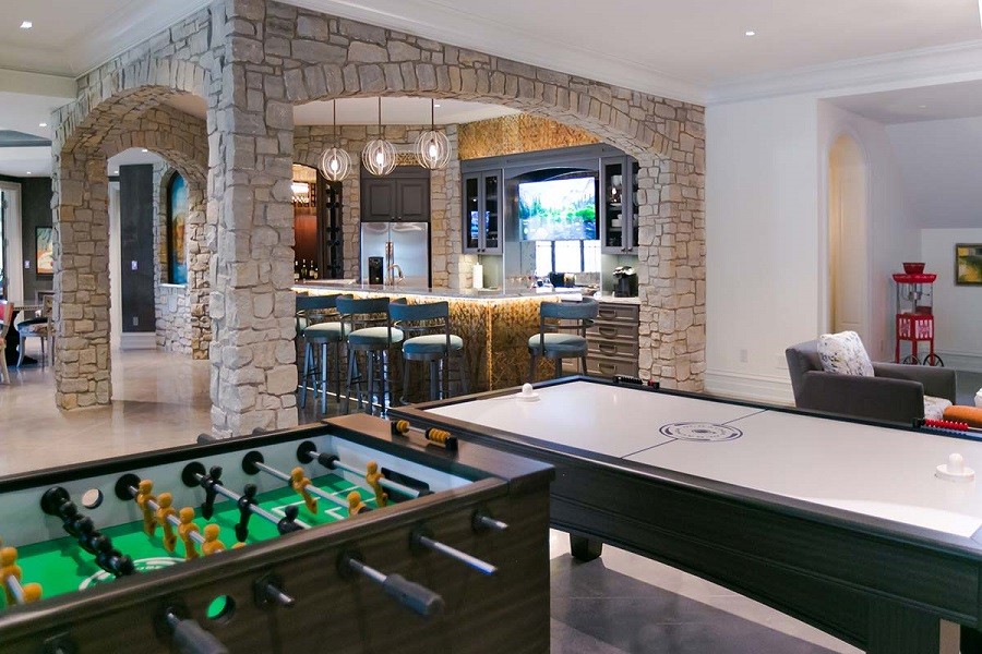 A brightly lit game room with a bar framed by stone arches. 