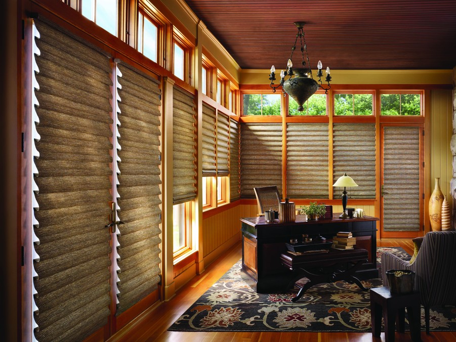 A home office with wooden motorized window treatments on the windows.