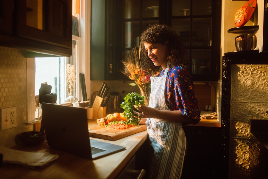 Woman in kitchen following a cooking video on laptop.