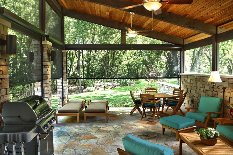 An outdoor patio with lighting, a grill, various seating areas, and partially lowered outdoor motorized shades. 