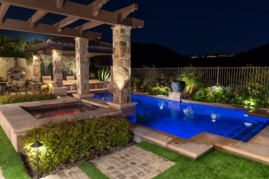 A backyard with beautiful lighting, a pool, and hidden Sonance speakers.