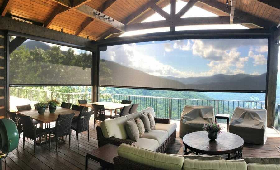 A covered outdoor patio with motorized shades from Progressive Screens partially lowered, offering sun protection while maintaining a scenic mountain view.