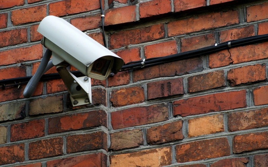 Outdoor security camera mounted on a red brick wall, with visible electrical wiring running along the building exterior.
